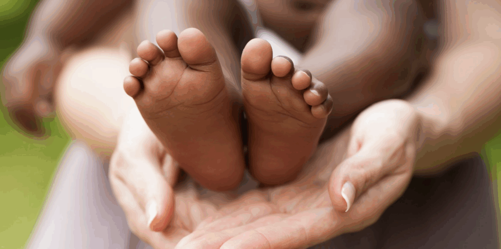 Baby feet held gently in an adult's hands, symbolizing love and connection in the context of adoption and family bonding.